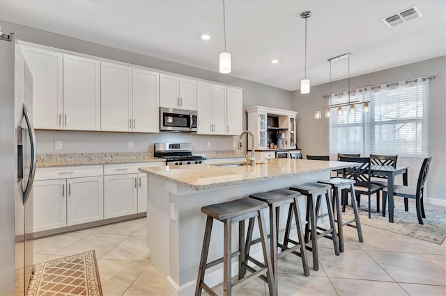 kitchen with hanging light fixtures, stainless steel appliances, white cabinets, and a center island with sink