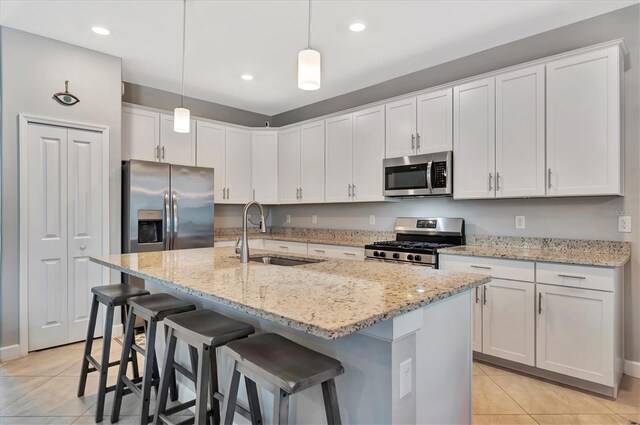 kitchen featuring appliances with stainless steel finishes, sink, an island with sink, light tile patterned flooring, and white cabinetry