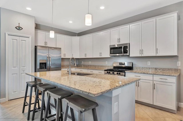 kitchen featuring appliances with stainless steel finishes, decorative light fixtures, white cabinetry, an island with sink, and sink