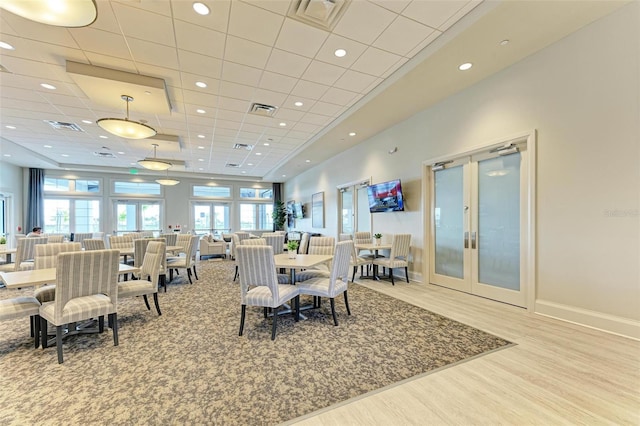 dining area with a drop ceiling, a towering ceiling, light hardwood / wood-style flooring, and french doors