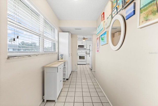 hallway with light tile patterned flooring, visible vents, baseboards, and a textured ceiling