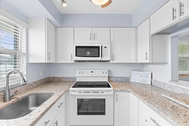 kitchen featuring white appliances, light stone counters, white cabinets, and a sink