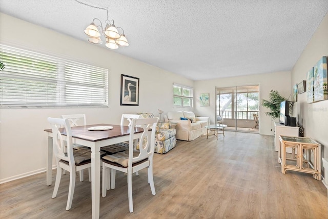 dining room with light wood finished floors, baseboards, a textured ceiling, and an inviting chandelier