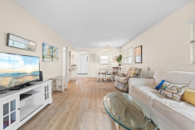 living area featuring a textured ceiling, light wood finished floors, and an inviting chandelier