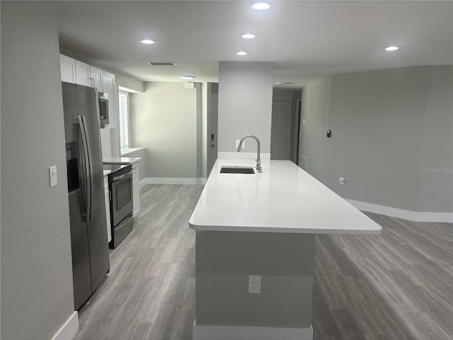 kitchen with appliances with stainless steel finishes, white cabinets, light wood-type flooring, an island with sink, and sink