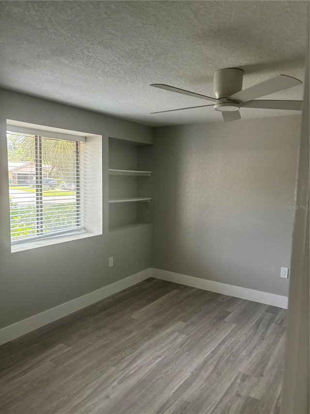 spare room featuring ceiling fan, wood-type flooring, a textured ceiling, and built in shelves