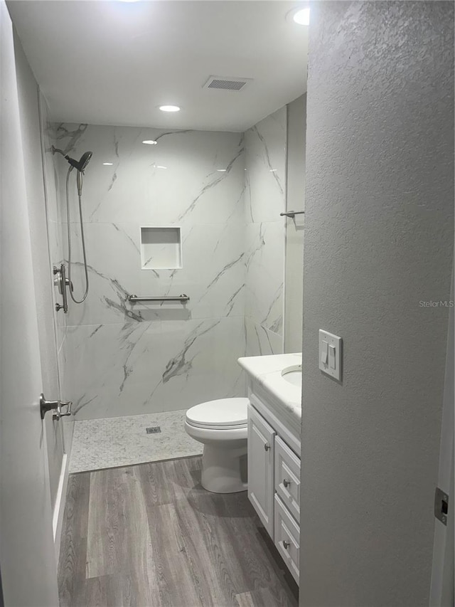 bathroom featuring vanity, a tile shower, toilet, and hardwood / wood-style flooring