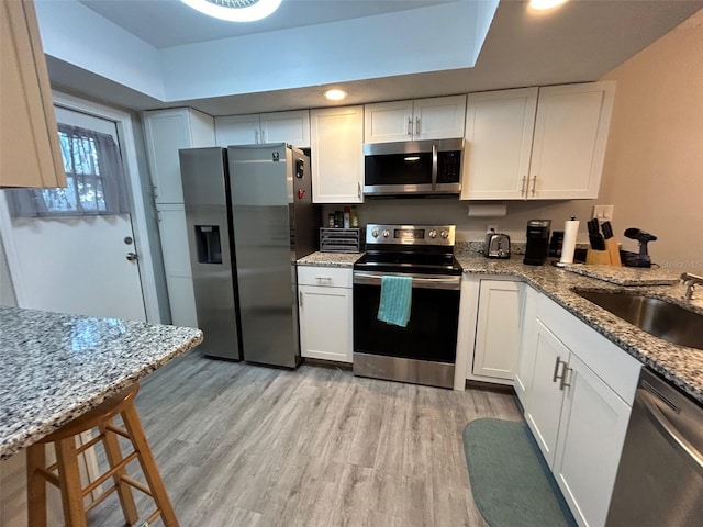 kitchen featuring light stone countertops, appliances with stainless steel finishes, light hardwood / wood-style floors, sink, and white cabinetry