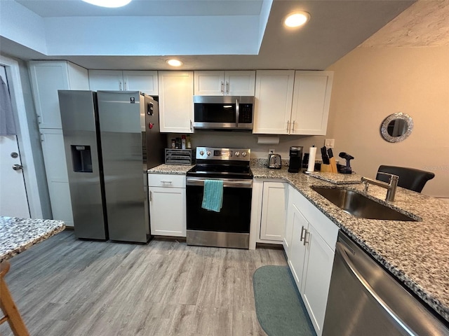 kitchen with appliances with stainless steel finishes, white cabinetry, light stone counters, and sink