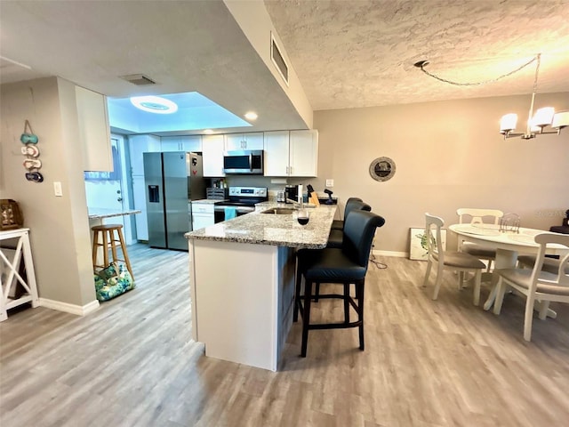 kitchen with light stone countertops, appliances with stainless steel finishes, kitchen peninsula, light wood-type flooring, and white cabinets