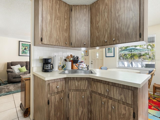 kitchen with light tile patterned floors, sink, a textured ceiling, kitchen peninsula, and backsplash