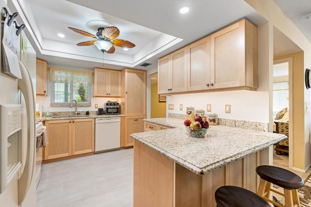 kitchen featuring white appliances, a raised ceiling, light brown cabinetry, kitchen peninsula, and a breakfast bar area