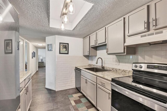 kitchen with backsplash, light stone counters, stainless steel appliances, sink, and decorative light fixtures