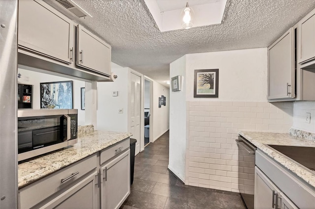 kitchen with gray cabinetry, light stone counters, stainless steel appliances, and a textured ceiling