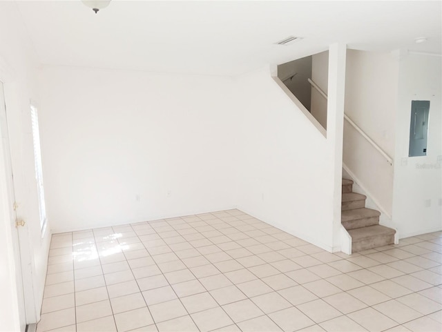 empty room with electric panel, stairway, visible vents, and light tile patterned floors