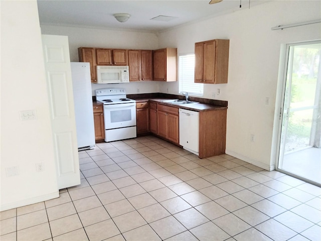 kitchen with white appliances, light tile patterned floors, brown cabinetry, a sink, and dark countertops
