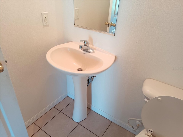 half bath with tile patterned floors, baseboards, toilet, and a sink