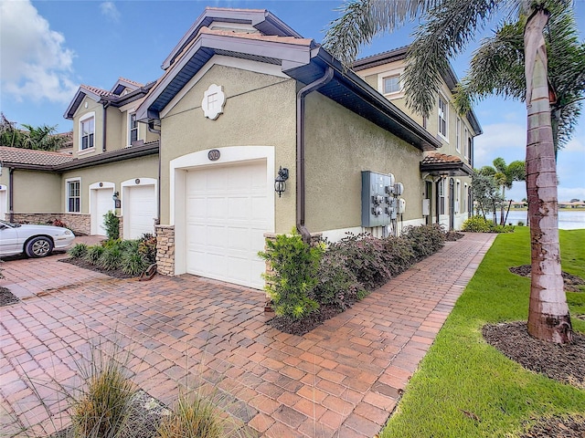 view of home's exterior with stone siding, decorative driveway, an attached garage, and stucco siding