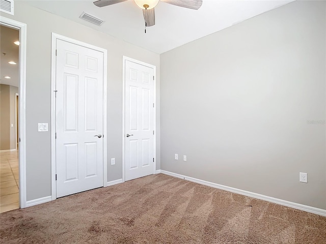 unfurnished bedroom with carpet flooring, two closets, and ceiling fan