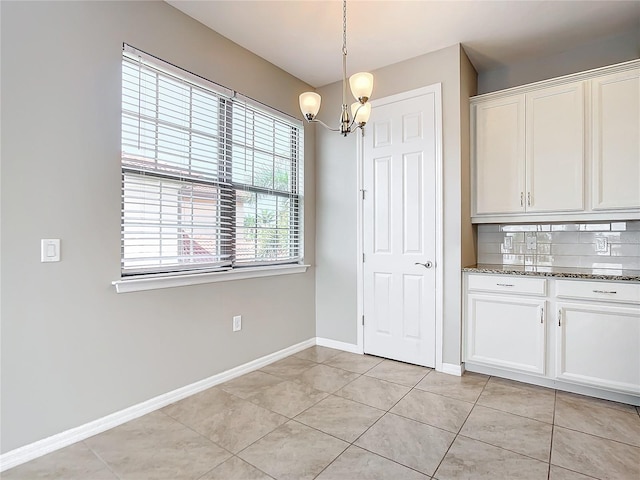 kitchen with dark stone counters, white cabinets, pendant lighting, light tile patterned floors, and tasteful backsplash