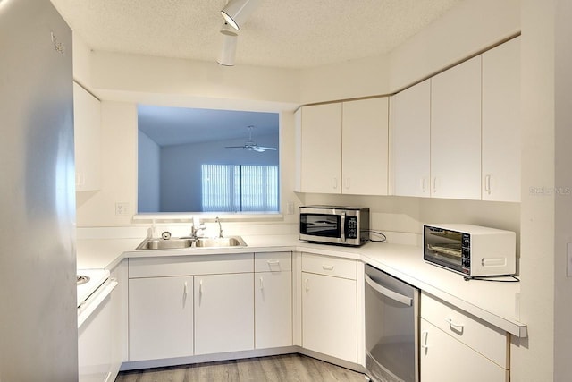 kitchen with a textured ceiling, stainless steel appliances, a sink, light countertops, and light wood-type flooring