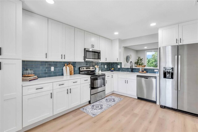 kitchen featuring white cabinetry, stainless steel appliances, decorative backsplash, and light wood-type flooring