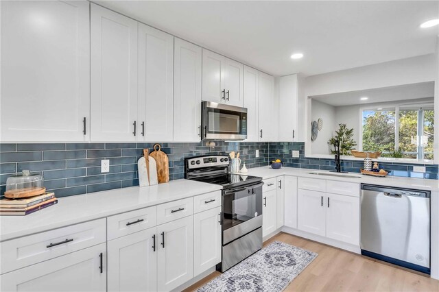 kitchen featuring appliances with stainless steel finishes, sink, white cabinets, and light wood-type flooring