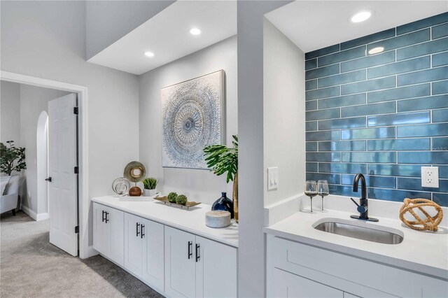 bar featuring sink, light colored carpet, and white cabinets