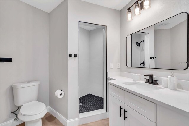 bathroom with hardwood / wood-style flooring, vanity, a tile shower, and toilet