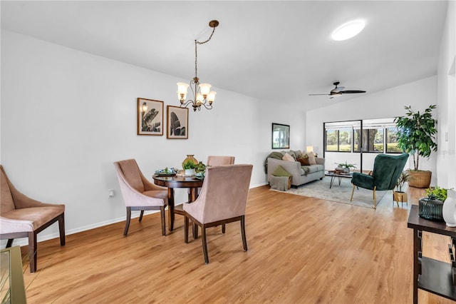 dining area with ceiling fan with notable chandelier, vaulted ceiling, and light hardwood / wood-style floors