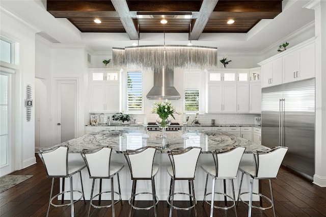 kitchen with coffered ceiling, wall chimney range hood, dark wood-type flooring, and built in fridge