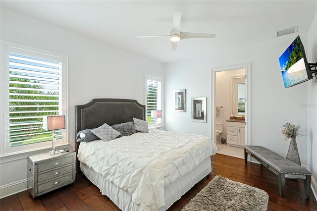 bedroom featuring ceiling fan, dark wood-type flooring, ensuite bathroom, and multiple windows