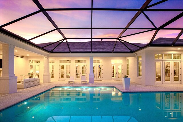 pool at dusk with glass enclosure, a patio, and french doors