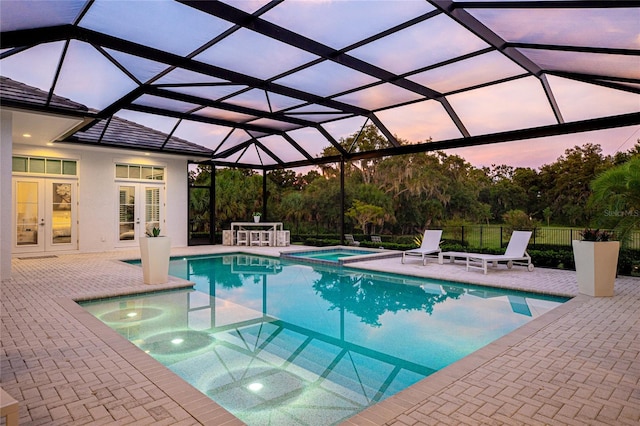 pool at dusk with a lanai, french doors, an in ground hot tub, and a patio