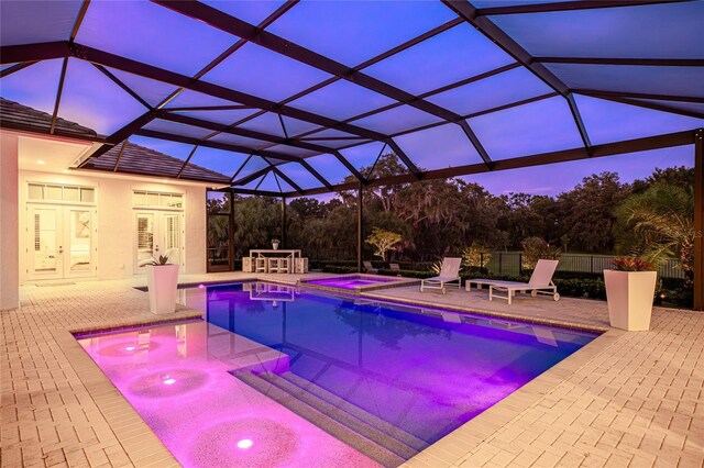 pool at dusk with glass enclosure, an in ground hot tub, and a patio