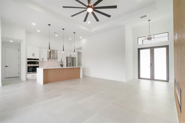 unfurnished living room featuring light tile patterned flooring, sink, a tray ceiling, french doors, and a high ceiling