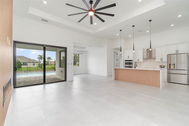 unfurnished living room featuring ceiling fan, a raised ceiling, light tile patterned floors, and a high ceiling