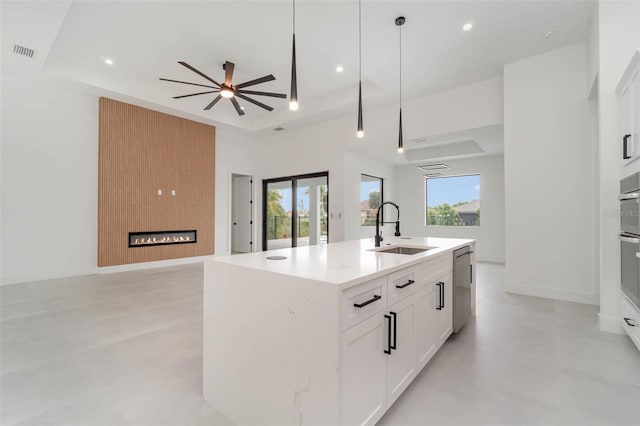 kitchen with a center island with sink, ceiling fan, sink, white cabinetry, and decorative light fixtures