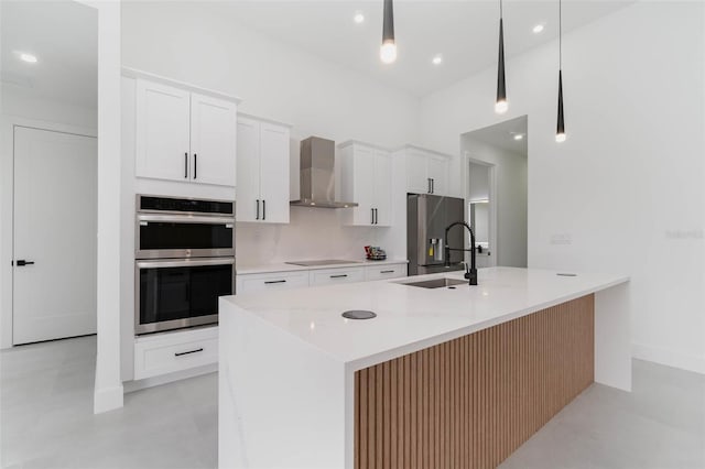 kitchen with stainless steel appliances, white cabinets, an island with sink, sink, and wall chimney range hood