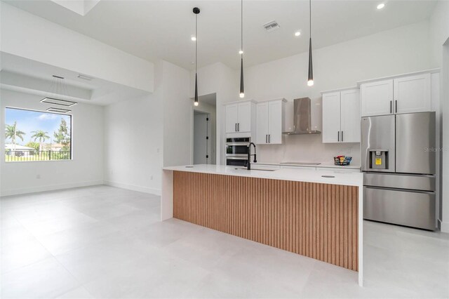 kitchen with light tile patterned floors, wall chimney range hood, stainless steel appliances, and white cabinetry