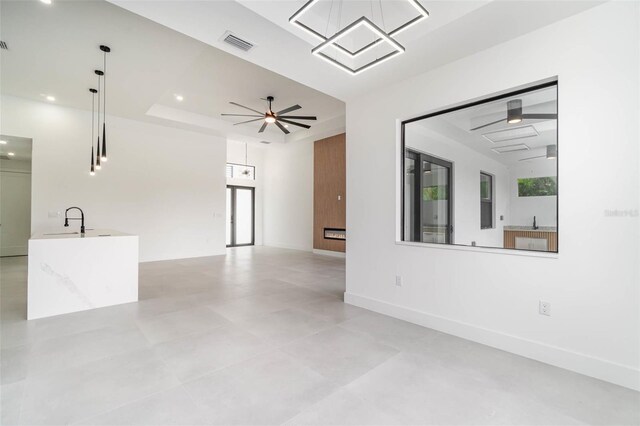 unfurnished living room with sink, ceiling fan, and a raised ceiling