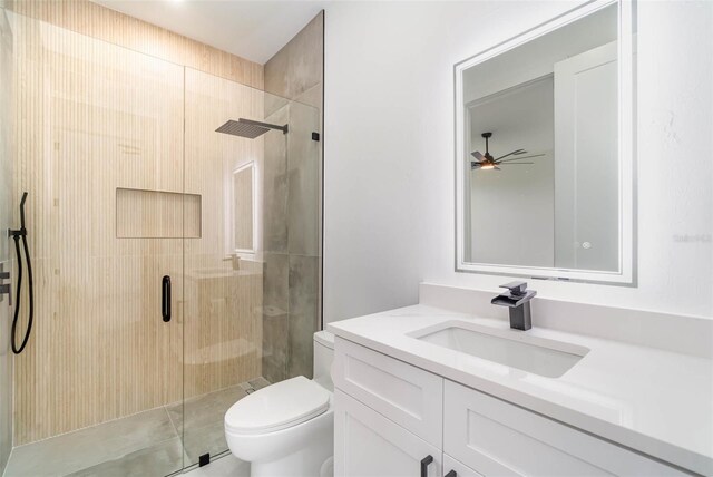 bathroom featuring ceiling fan, a shower with door, vanity, and toilet