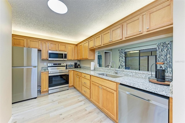 kitchen with appliances with stainless steel finishes, sink, light wood-type flooring, light stone countertops, and a textured ceiling