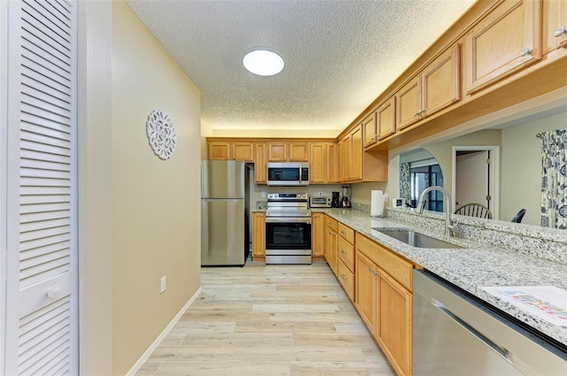 kitchen with light hardwood / wood-style flooring, a textured ceiling, light stone countertops, appliances with stainless steel finishes, and sink