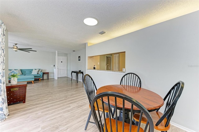 dining area with a textured ceiling, sink, light wood-type flooring, and ceiling fan