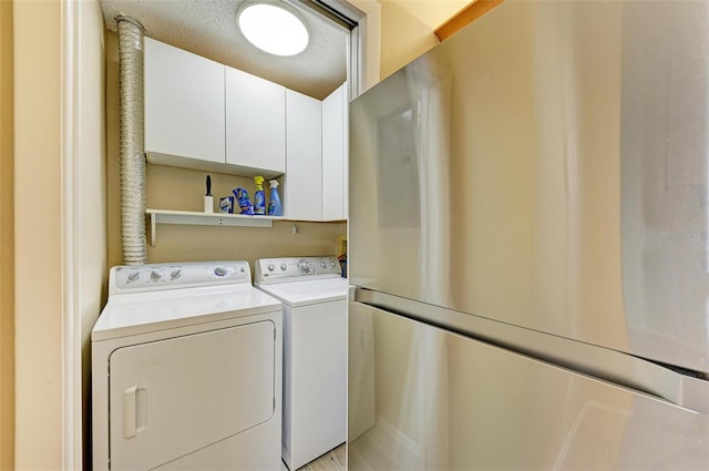 laundry area featuring washer and dryer, a textured ceiling, and cabinets