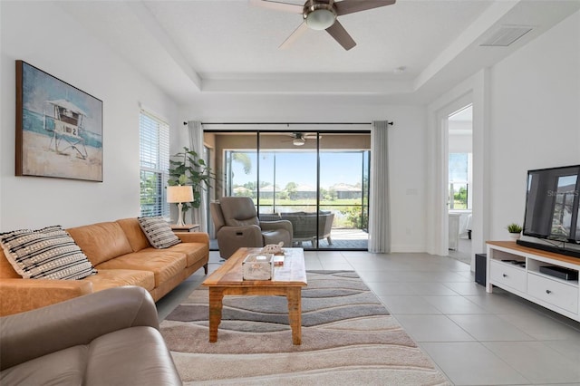 tiled living room with ceiling fan, plenty of natural light, and a tray ceiling