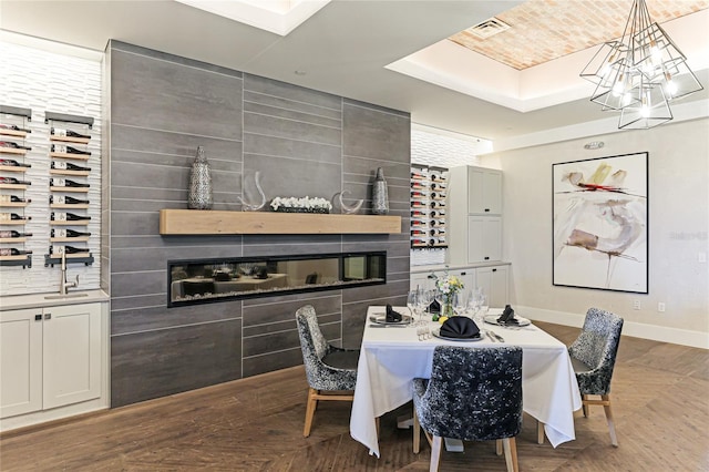 dining area with a notable chandelier, a large fireplace, a tray ceiling, and parquet flooring