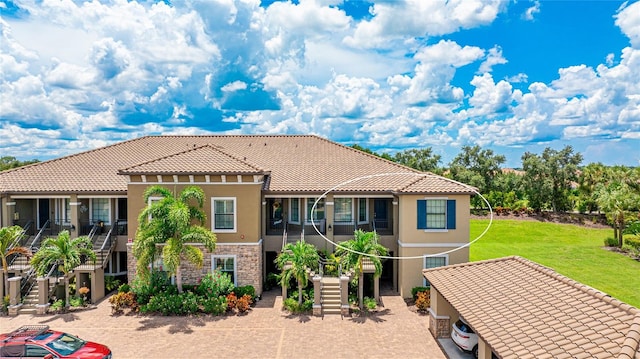 mediterranean / spanish-style house featuring a tile roof, stairs, stone siding, stucco siding, and a front yard