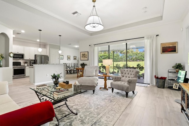 living room with light wood-type flooring, a raised ceiling, and ornamental molding